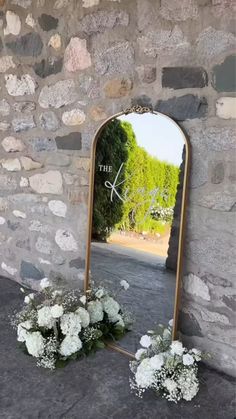 a large mirror sitting on top of a stone wall next to flowers and plants in front of it