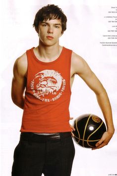 a young man holding a basketball in his right hand and wearing a red tank top