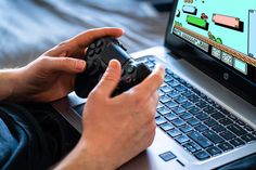 a man is holding a video game controller in front of his laptop