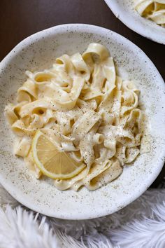 two white bowls filled with pasta and lemon slices