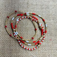 three red, white and gold beaded bracelets on a piece of burlied fabric