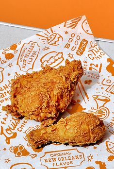 two fried chicken pieces sitting on top of a paper wrapper next to each other