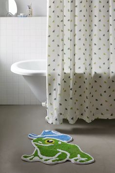 a green frog rug sitting on the floor in front of a bathtub and shower curtain