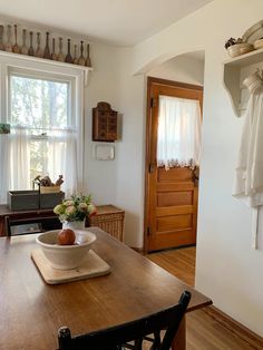 a wooden table topped with a bowl filled with fruit next to a window covered in curtains