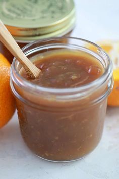 an orange next to a jar of jam with a wooden spoon