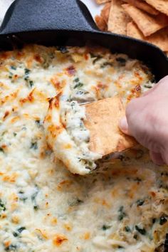 a hand dipping a tortilla chip into a skillet filled with cheese and spinach