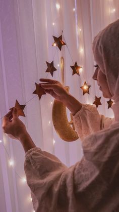 a woman in a white dress is holding stars and a crescent hanging from the curtain