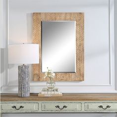 a table with a lamp, mirror and vase on it in front of a white wall