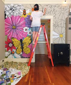 a person standing on a ladder in front of a wall with flowers and butterflies painted on it