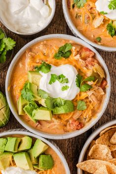 four bowls filled with soup, tortilla chips and sour cream on a table