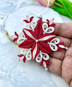 a hand holding a red and white ornament on top of a piece of paper