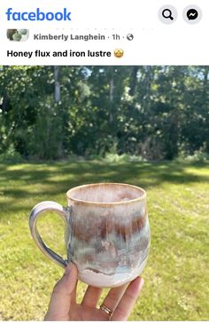 someone is holding up a coffee mug in the grass with trees in the back ground