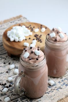 two mason jars filled with hot chocolate and marshmallows on a tablecloth