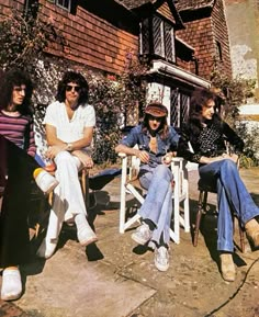 four people sitting on chairs in front of a house