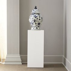 a white and blue vase sitting on top of a pedestal in front of a wall