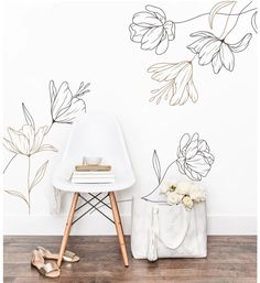 a white chair sitting in front of a wall with flowers on it and a purse next to it