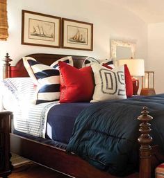 a bed with blue and red pillows on it in a bedroom next to two framed pictures