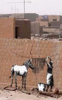 a zebra painted on the side of a brick wall next to a man with a bucket