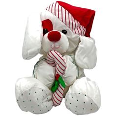 a white stuffed dog wearing a santa hat and holding a candy cane in its mouth