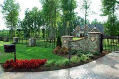 a gated entrance to a home surrounded by lush green grass and trees with red flowers in the foreground