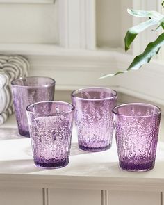 four purple glass cups sitting on top of a table next to a plant in a vase