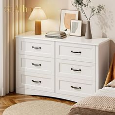 there is a white dresser with pictures on it and a lamp next to the dresser