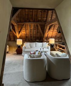 a living room filled with white furniture next to a wooden ceiling covered in wood beams