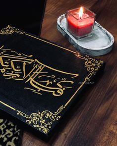 a lit candle sits on top of a black and gold book with an intricate design