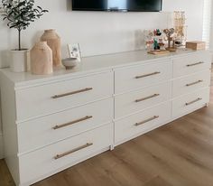 a tv mounted on the wall above a white dresser with gold handles and brass pulls