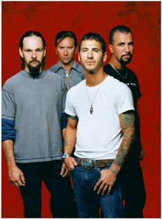 a group of men standing next to each other in front of a red wall with one man looking at the camera