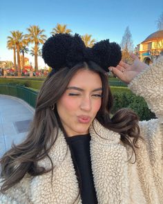 a woman with long hair wearing a mickey mouse ears headband in front of a park