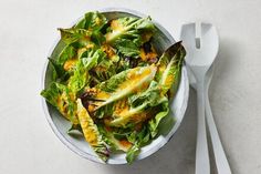 a salad with lettuce and cheese in a white bowl next to a fork