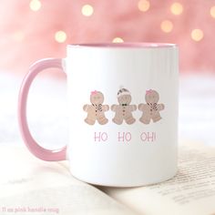 a pink and white coffee mug with two gingerbreads on it sitting next to an open book