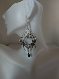 Unveil your daring side with our spellbinding Gothic Bat Earrings. Crafted in the captivating Tibetan silver style, these unique earrings feature intricately designed bats and a raised connector, all adorned with a mesmerizing black teardrop crystal. Embrace the allure of the night with our exquisitely detailed bat-shaped earrings, symbolizing mystery and transformation for those who appreciate the enigmatic. Each pair of Gothic Bat Earrings is meticulously handcrafted with skill and passion, ensuring a high level of artistry and quality. Their darkly stylish and bold design allows them to seamlessly complement various outfits, from casual wear to formal attire. For those seeking an accessory that stands out from the crowd, our Gothic Bat Earrings are the perfect choice to draw attention a Fantasy Metal Earrings For Halloween, Gothic Metal Plug Earrings, Silver Gothic Plug Earrings, Gothic Metal Earrings For Halloween, Gothic Metal Plug Earrings For Party, Gothic Earrings For Halloween, Silver Fantasy Earrings For Halloween, Gothic Plug Earrings For Halloween, Halloween Fantasy Earrings For Pierced Ears