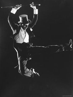 a black and white photo of a man with a top hat on jumping in the air