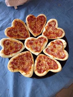 heart shaped pizzas arranged in the shape of hearts on a black plate with blue cloth