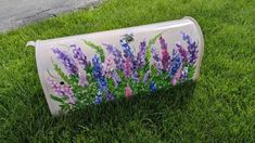 a painted mailbox sitting in the grass with purple flowers on it's side