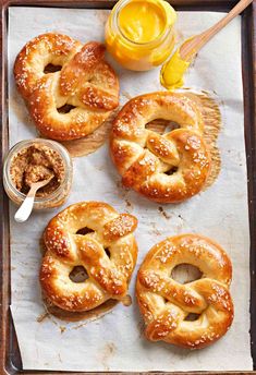 four pretzels sitting on top of a baking sheet next to a jar of honey