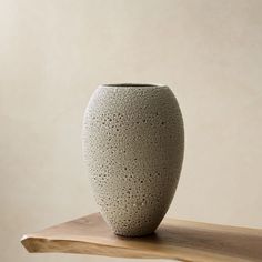 a white vase sitting on top of a wooden shelf in front of a beige wall