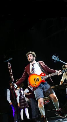 a man with a guitar standing on stage in front of other men and one woman