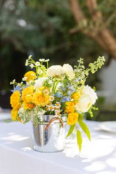 a vase filled with yellow and white flowers on top of a table next to a tree