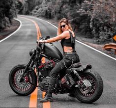 a woman sitting on top of a motorcycle in the middle of an empty road with trees and bushes behind her