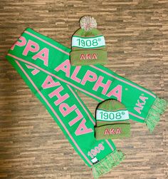 two green scarfs with pink and white letters on them sitting on top of a wooden floor