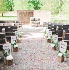 an outdoor ceremony with wooden signs and flowers on the aisle, surrounded by stone walls