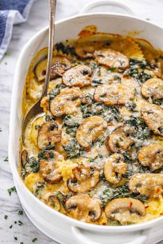 a casserole dish with mushrooms and spinach in a white baking dish on a marble surface