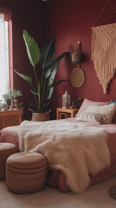 a bedroom with red walls and white fur on the bed, two stools and a plant