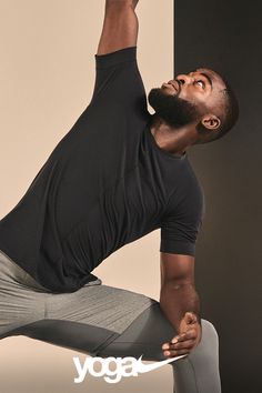 a man in black shirt and grey pants doing yoga pose with his hands up to the side