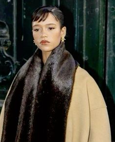 a woman wearing a fur stoler and earring standing in front of a building