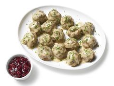 a white plate topped with meatballs next to a bowl of cranberry sauce