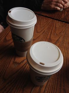 two coffee cups sitting on top of a wooden table next to each other with their lids down